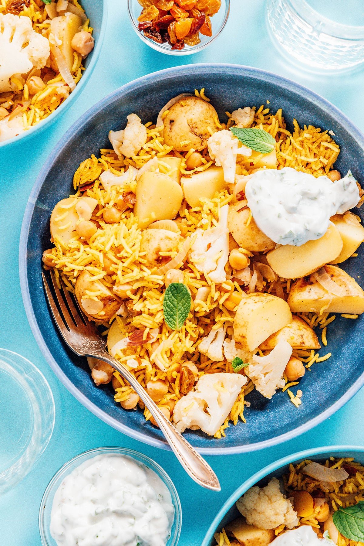 A blue bowl filled with vegetable biryani and topped with minted yogurt