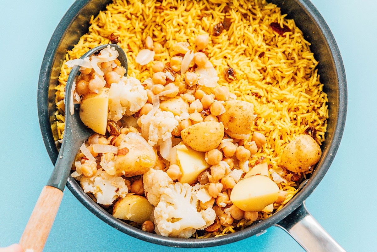 A spoon scooping from a skillet filled with veggie biryani