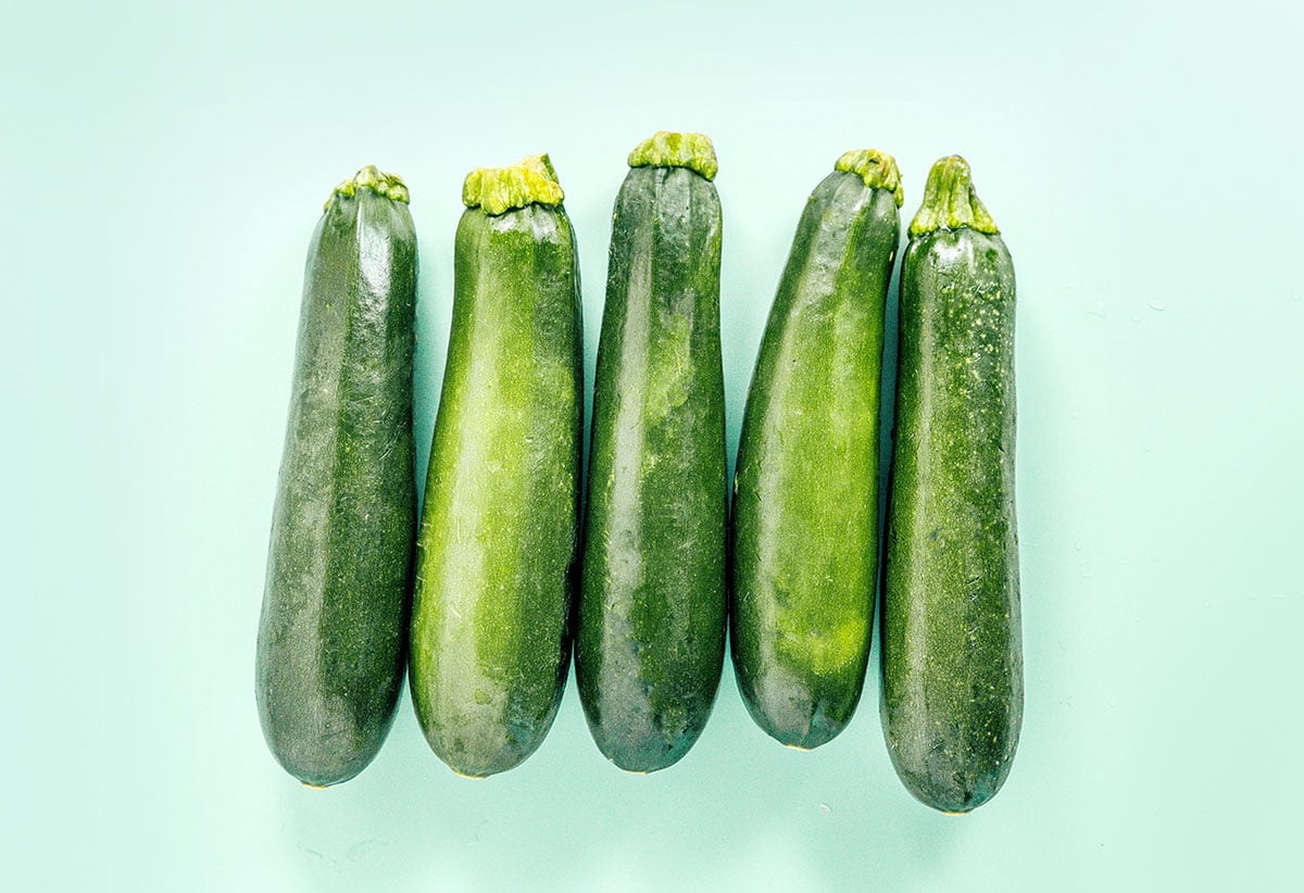 Five zucchini on a light aqua surface.
