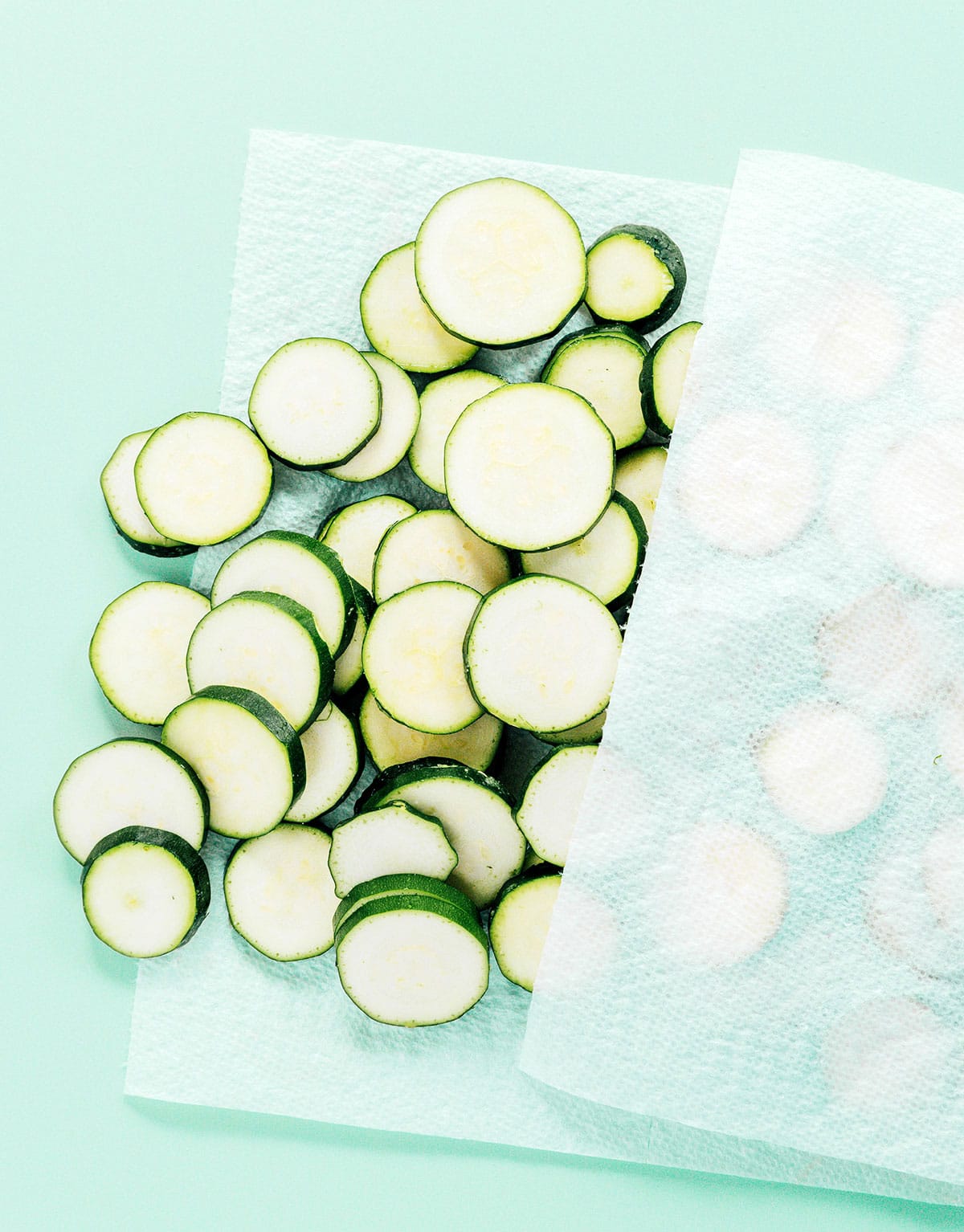 Zucchini rounds being pressed between layers of paper towel.