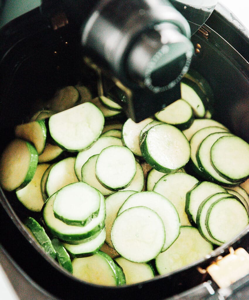 Raw zucchini rounds in the basket of an air fryer.