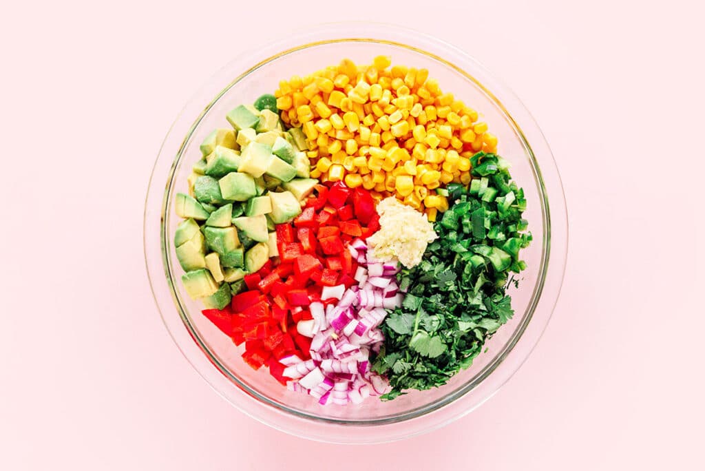 Diced ingredients for avocado corn salsa in a clear mixing bowl.