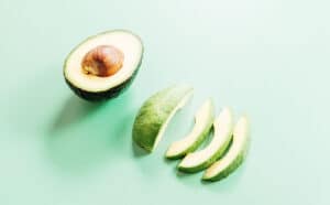 A halved avocado with the pit and four avocado slices, perfect for making avocado fries, are arranged on a light green background.