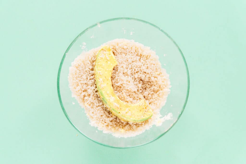 An avocado slice in a small bowl of panko bread crumbs.