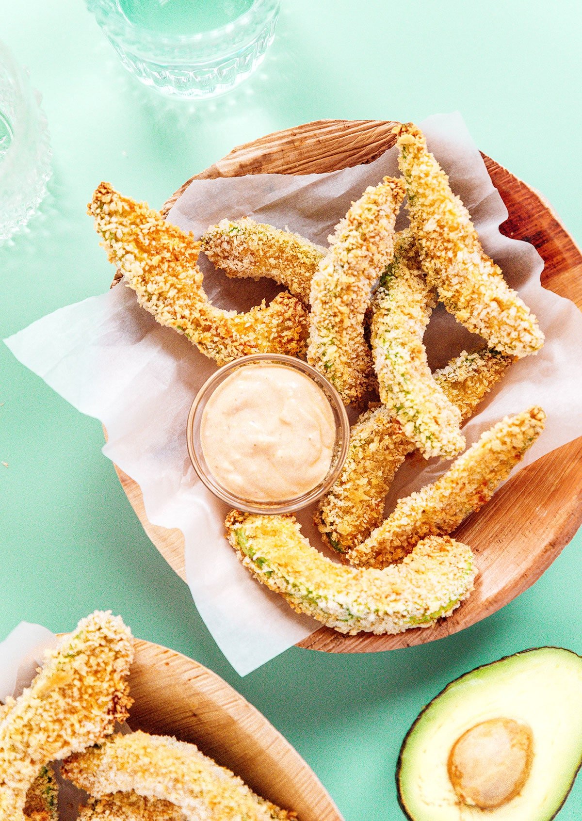 Baked avocado fries and a cup of dipping sauce in a wooden bowl.