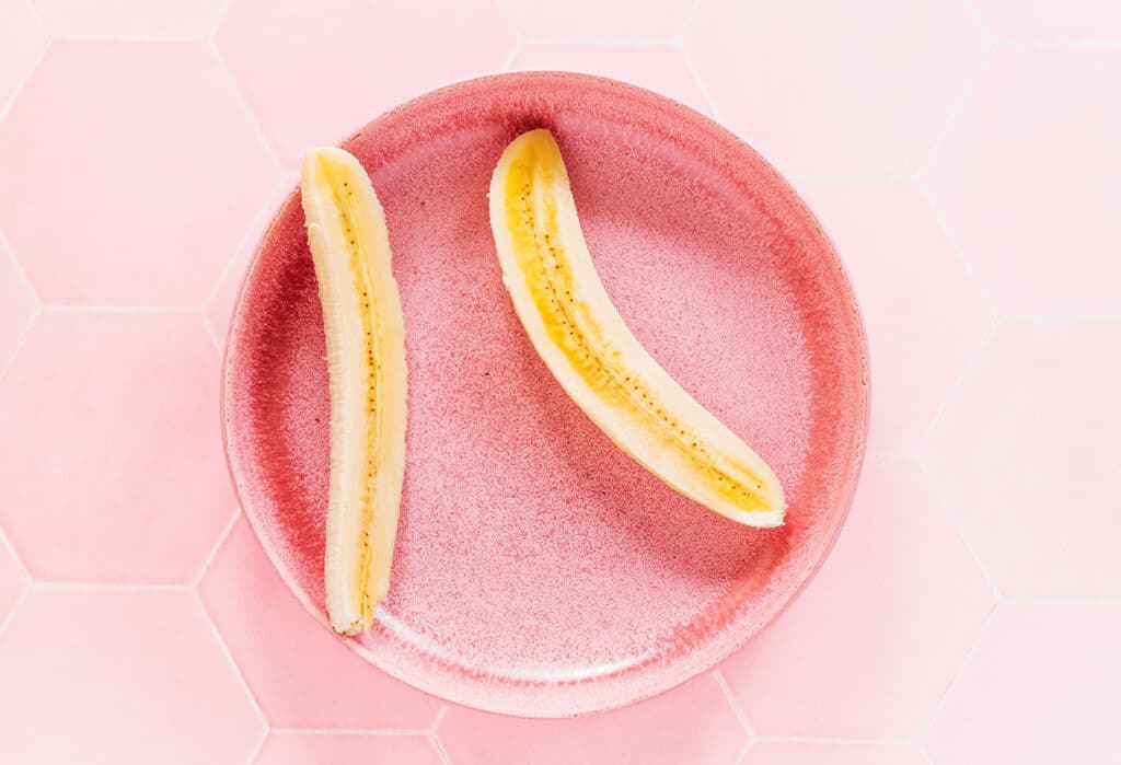 A peeled banana split lengthwise and set in a shallow pink bowl.