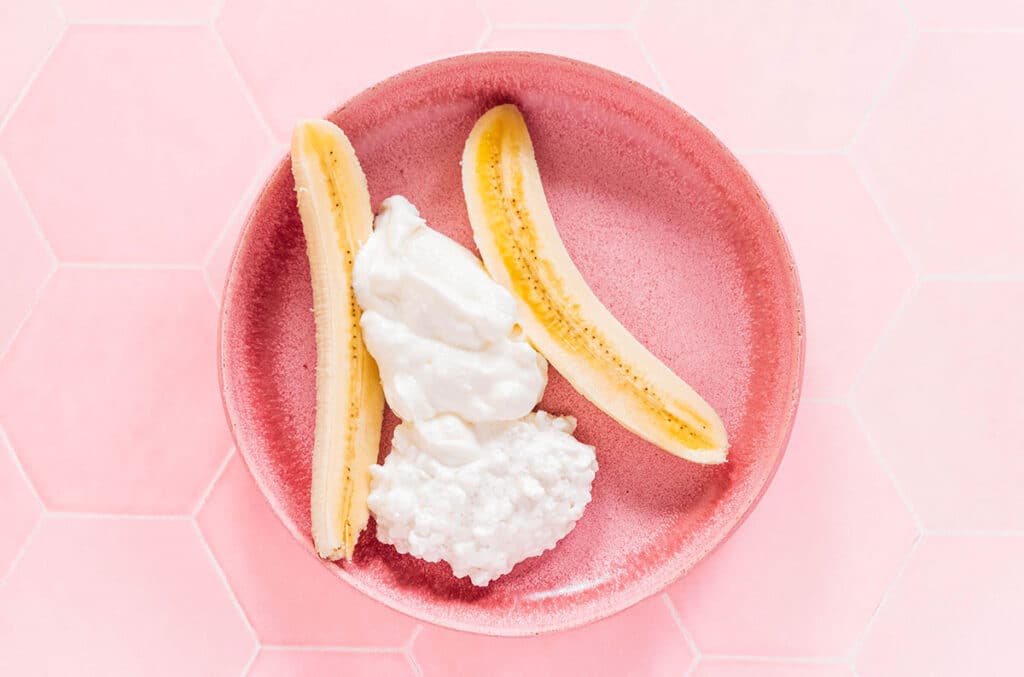 Cottage cheese and yogurt spooned into a split banana in a shallow bowl.