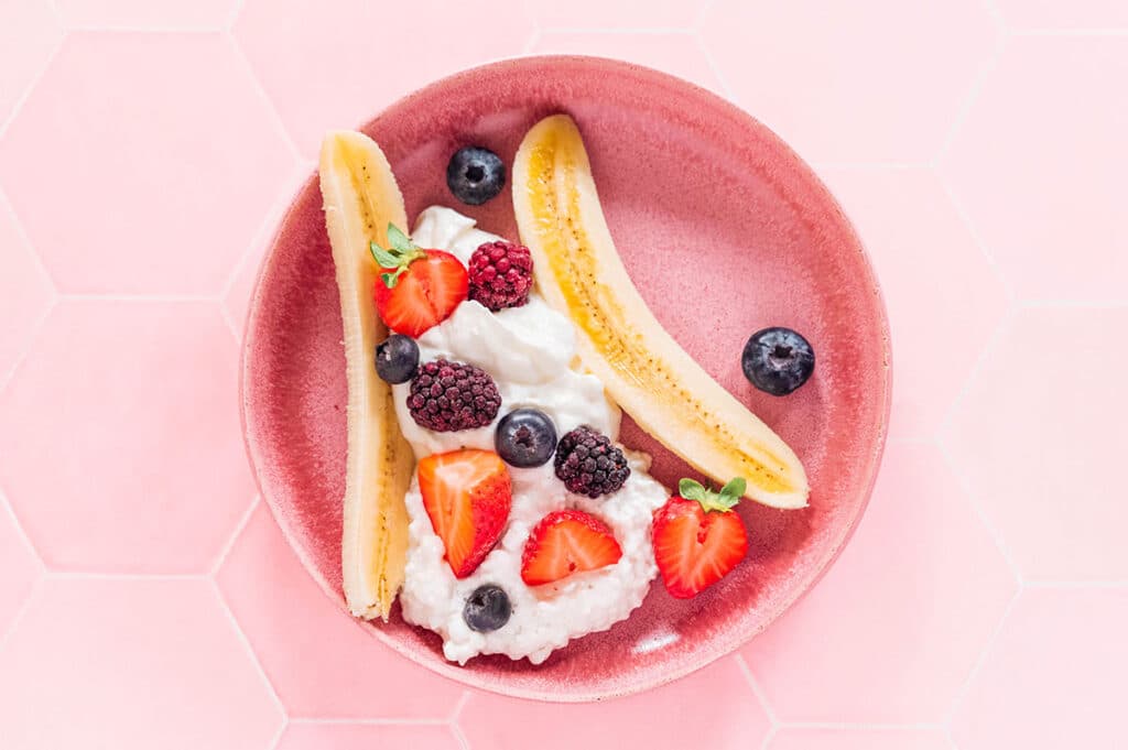 Berries sprinkled over yogurt between a banana split lengthwise.