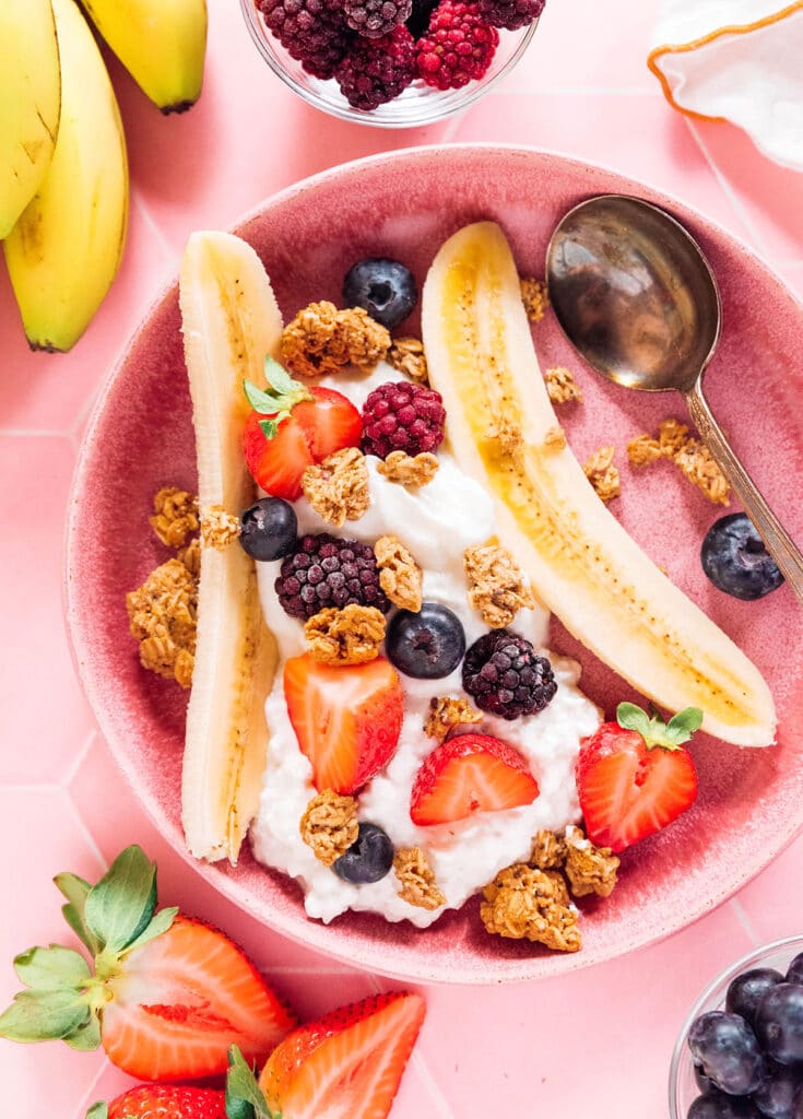 A split open banana with cottage cheese and yogurt topped with berries and granola.