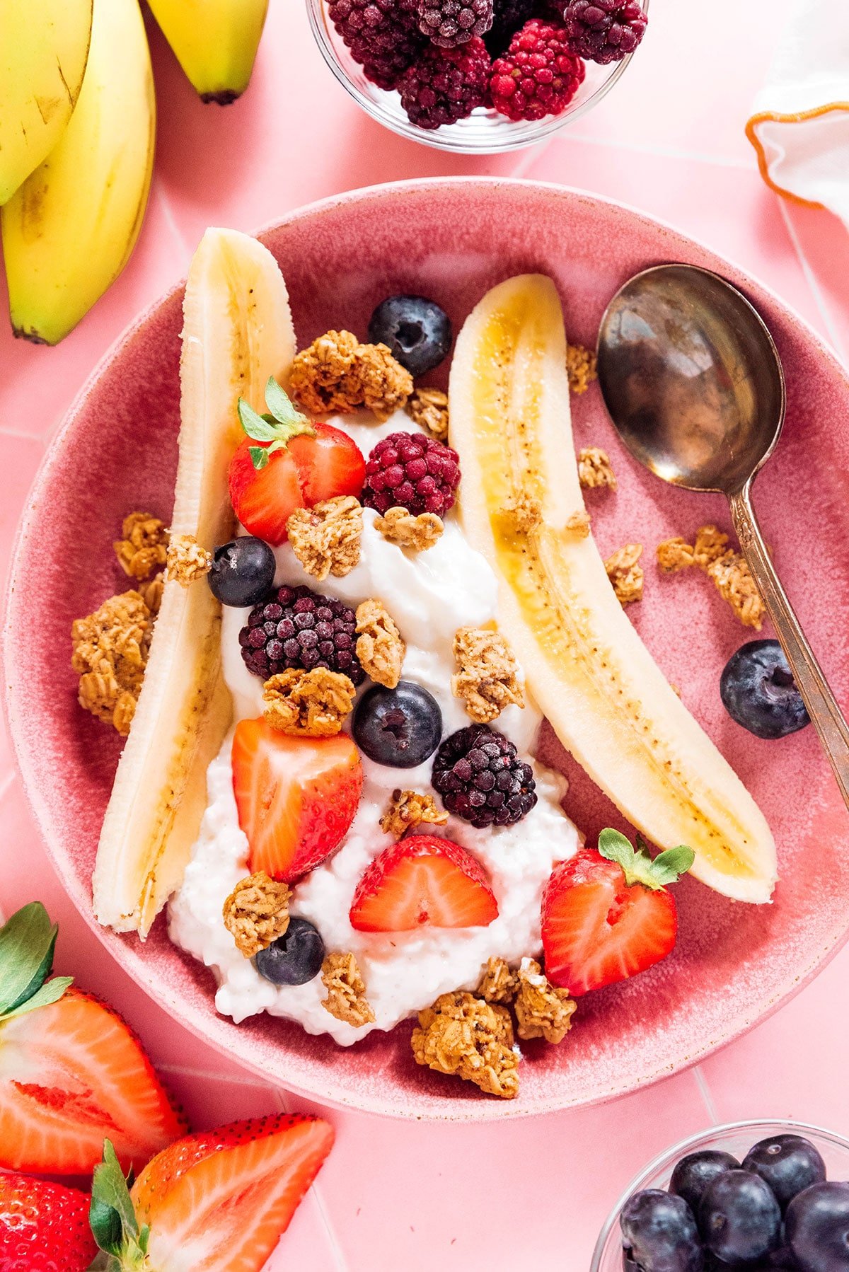 A split open banana with cottage cheese and yogurt topped with berries and granola.