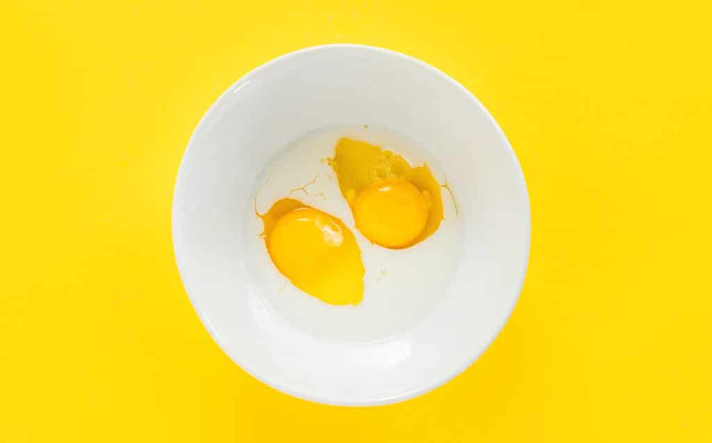 Cracked egg and milk in a small white mixing bowl.