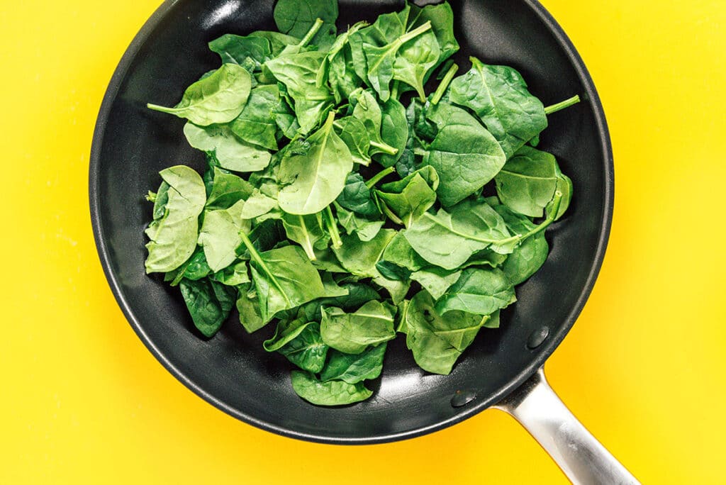 A black skillet filled with fresh baby spinach.