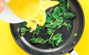 Eggs being poured into the pan with the spinach.