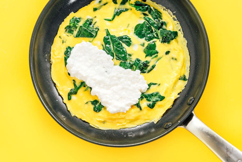 Cottage cheese set in the middle of an egg and spinach omelette in a skillet.