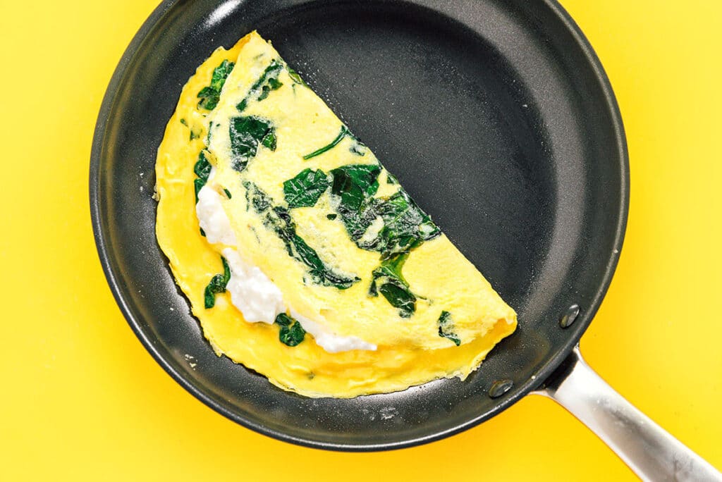A cottage cheese omelette folded in half in a black skillet.