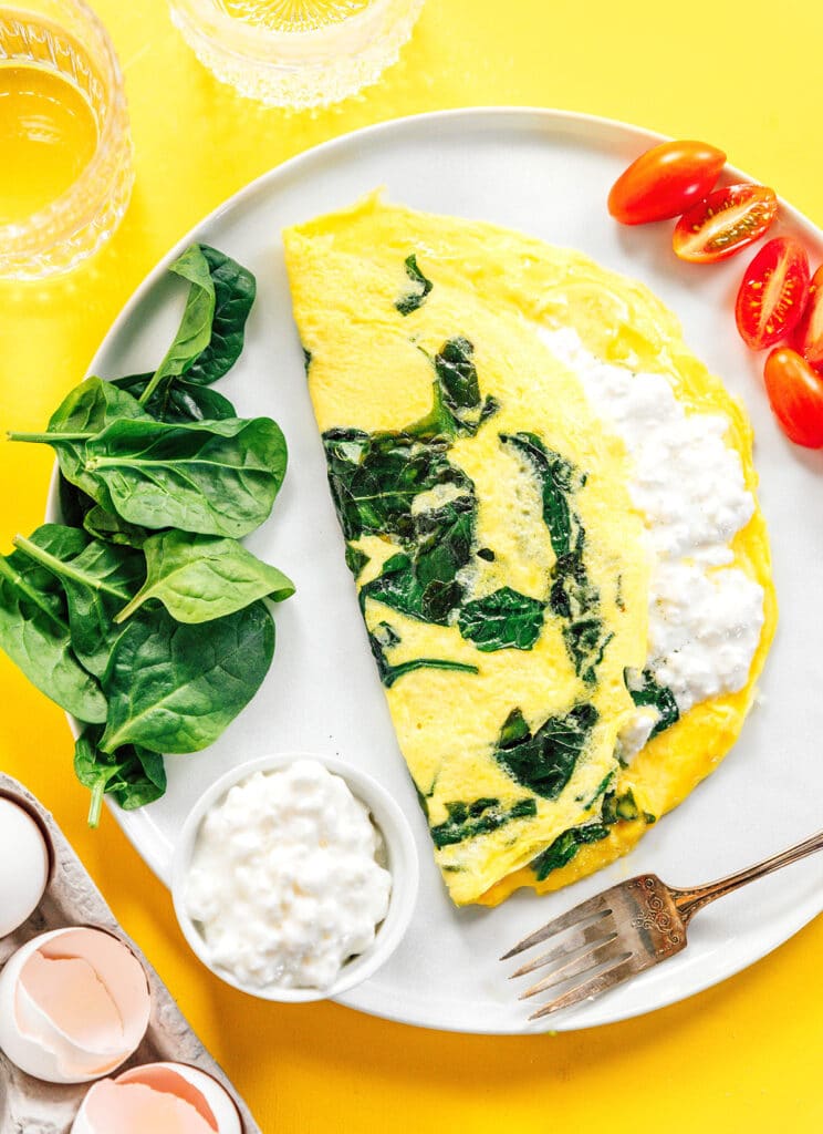 Cottage cheese and spinach omelette on a white plate with tomatoes and spinach aside.