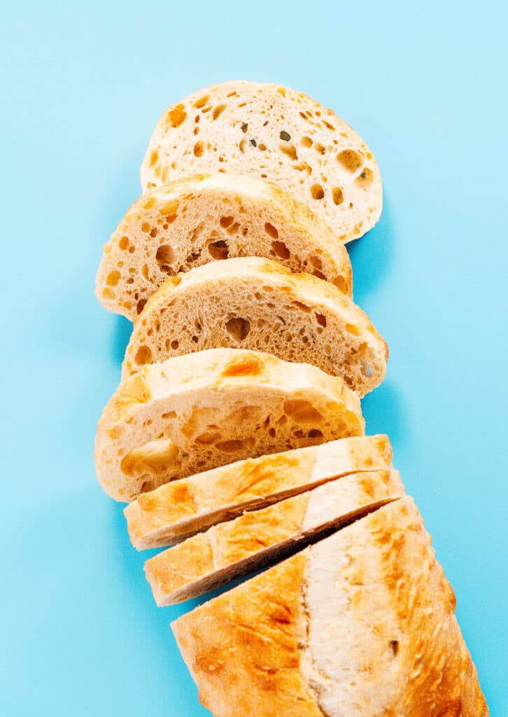 A baguette that is half sliced and spread out on a blue backdrop. 