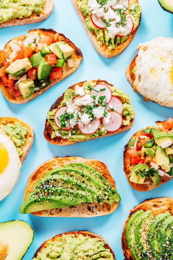 All five types of avocado toast laid out on a blue back drop.