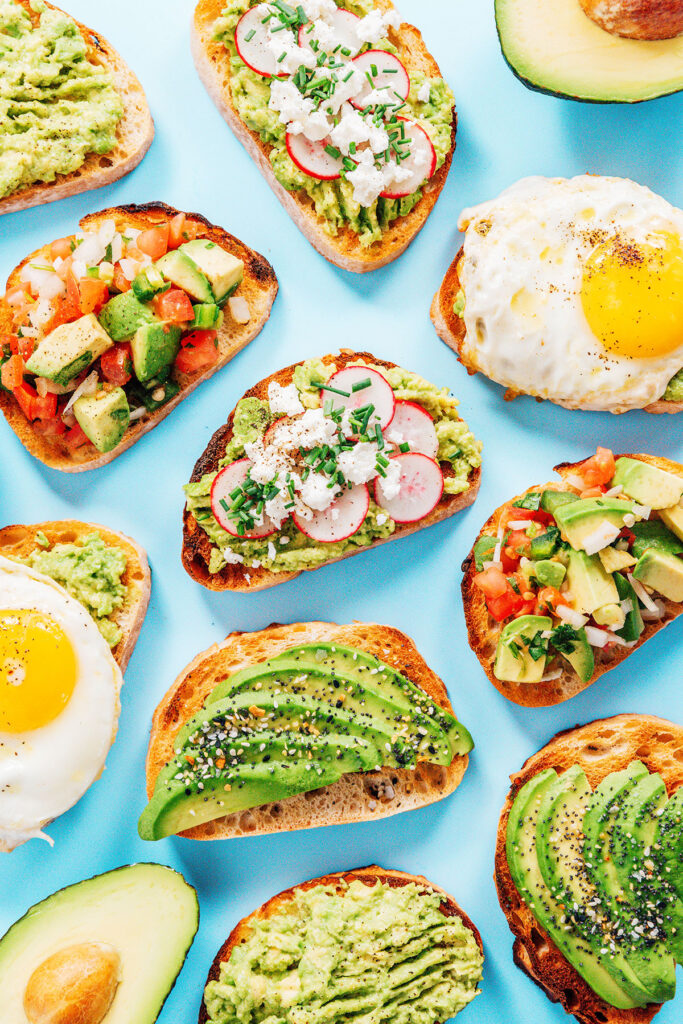 Pieces of different types of avocado toast laid out on a blue backdrop.