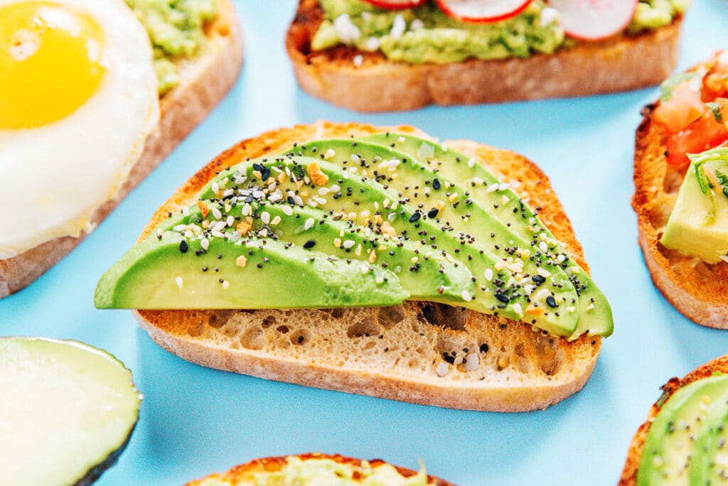 A slice of everything bagel avocado toast surrounded by other avocado toast variations.