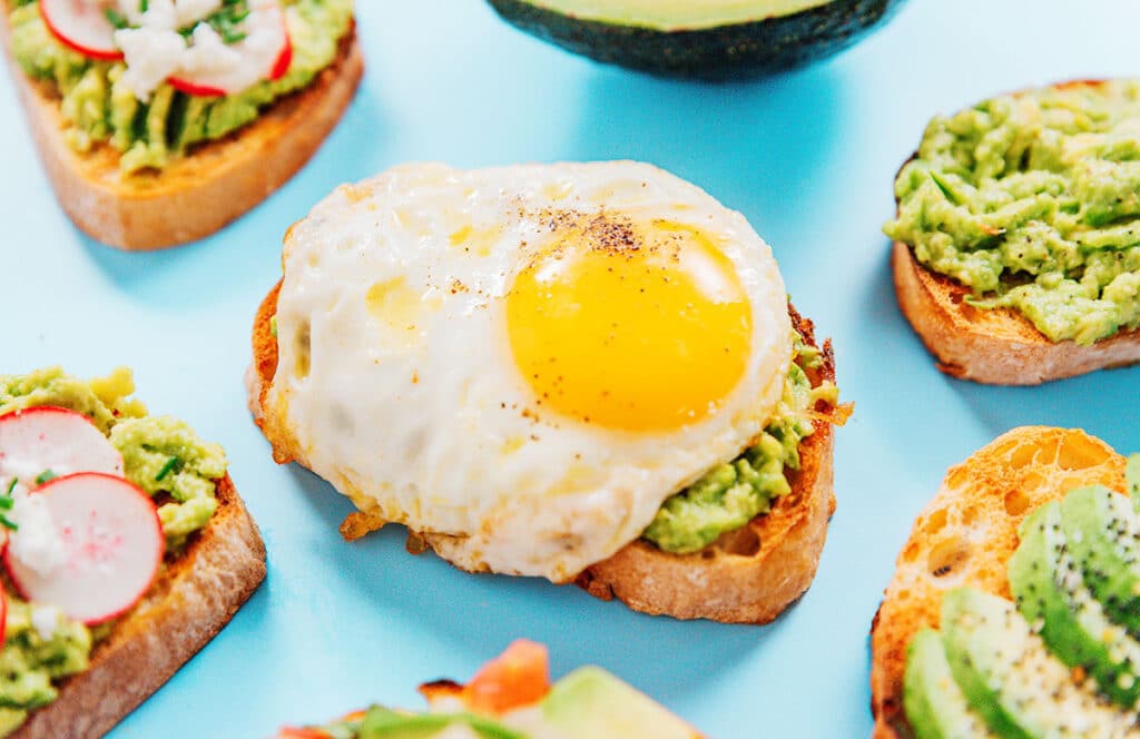 A slice of egg avocado toast surrounded by other variations of avocado toast.