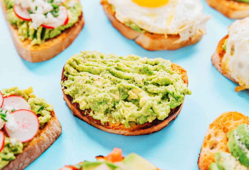 The classic toast with a piece of toast and mashed avocado and lemon juice surrounded by other avocado toasts.