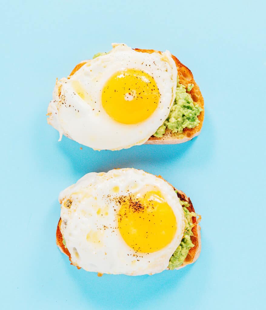 Two slices of egg avocado toast with mashed avocado and an over easy fried eg on each slice of toast.