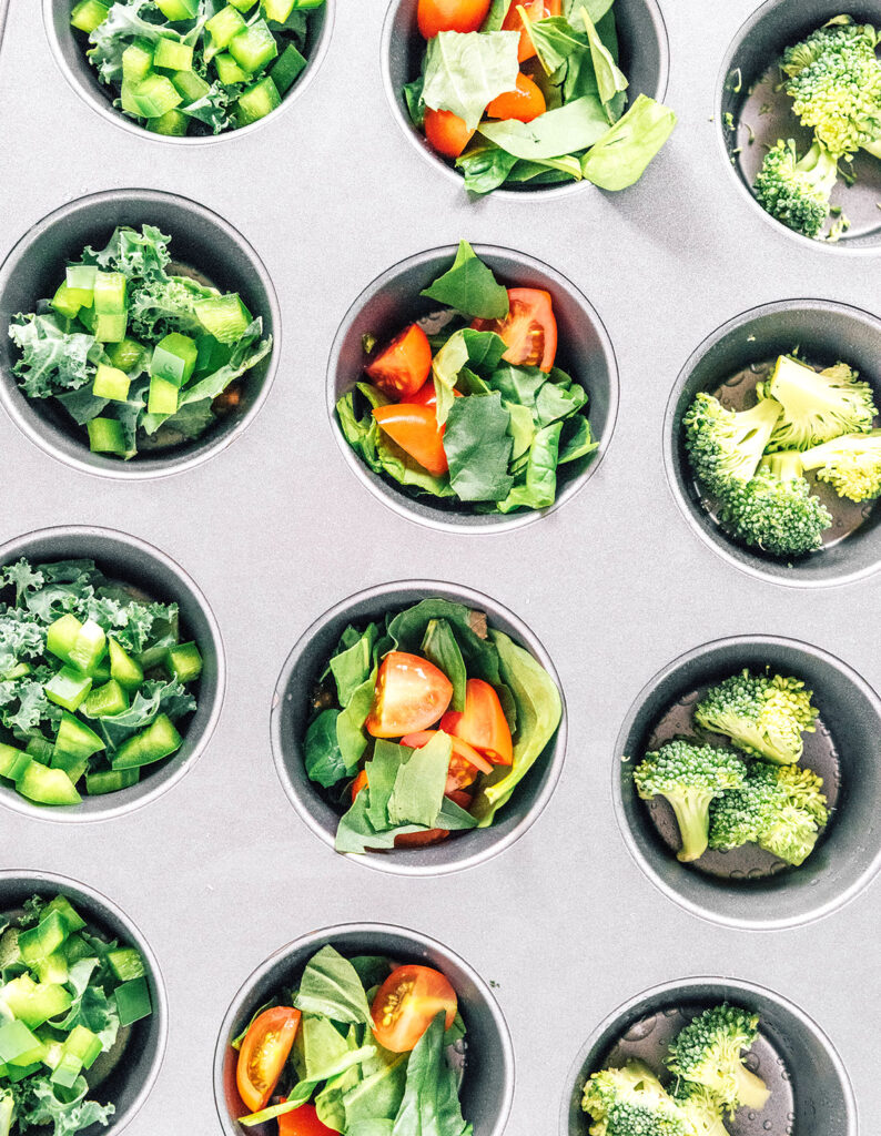 Green veggies filling the cups of a greased metal muffin tin.