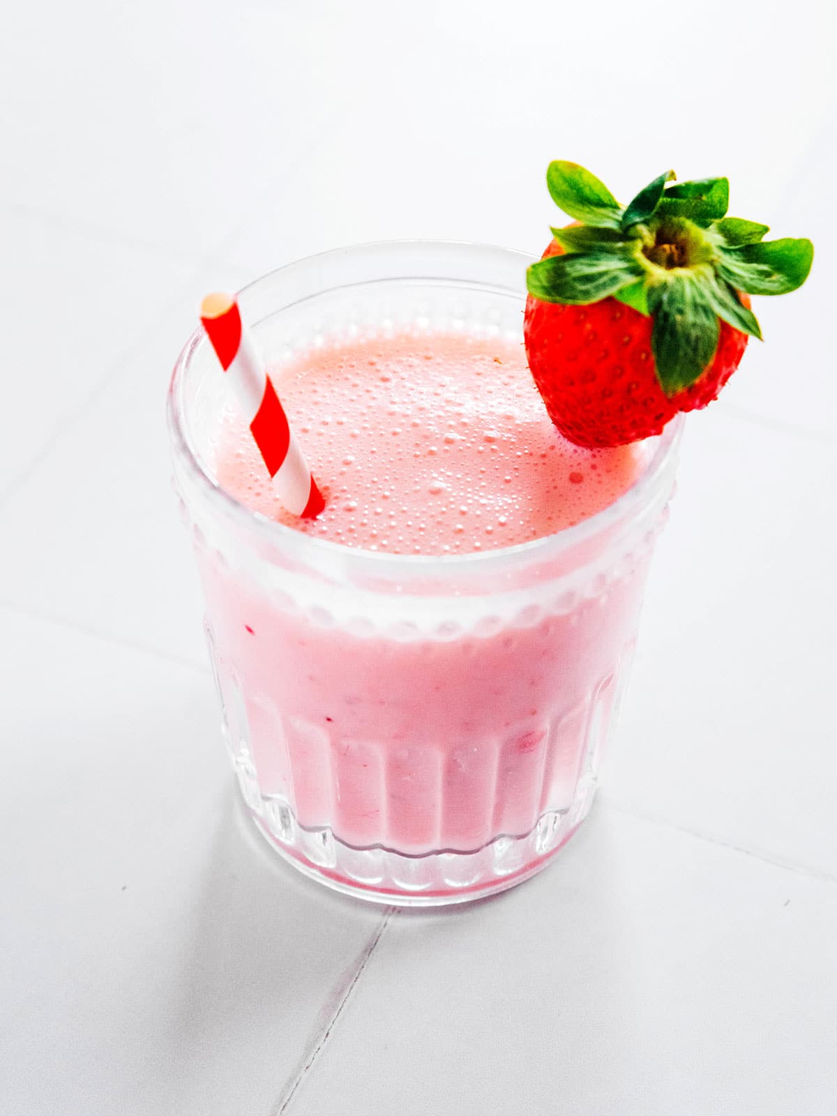 A glass of strawberry kefir with a straw and fresh strawberry on the rim.