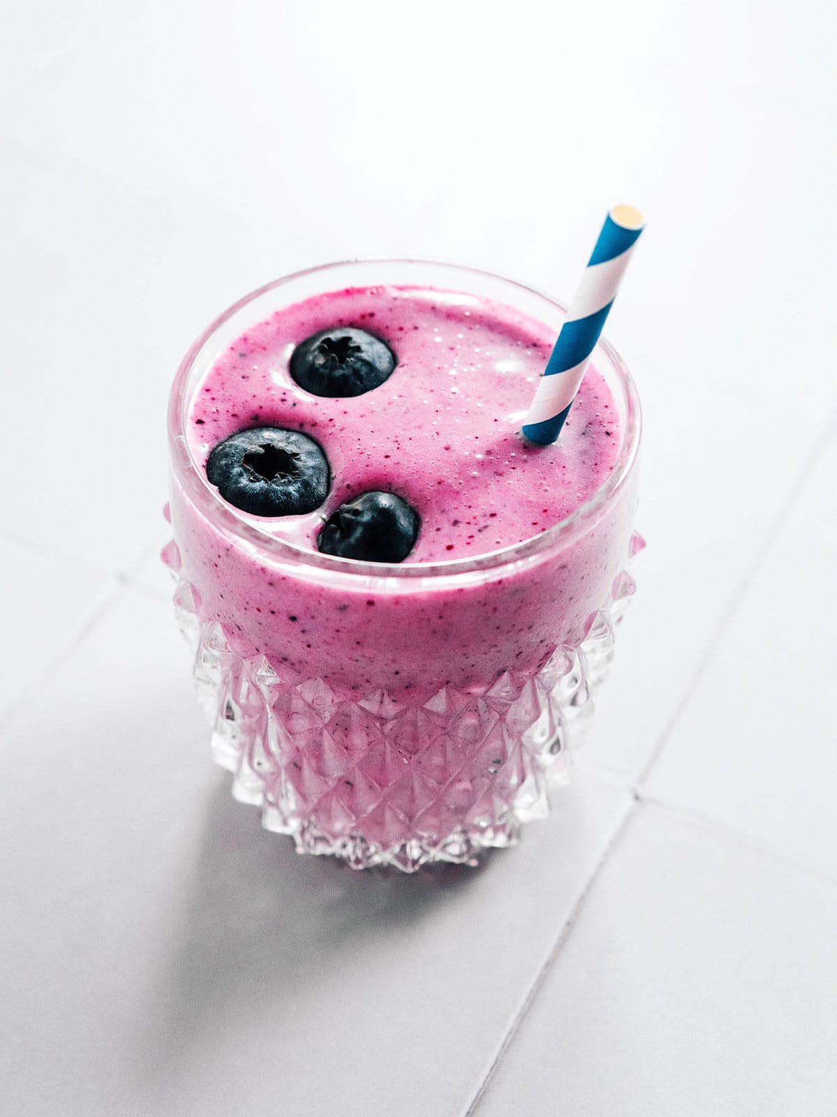 A glass of blueberry kefir with a straw and some fresh blueberries floating on top.