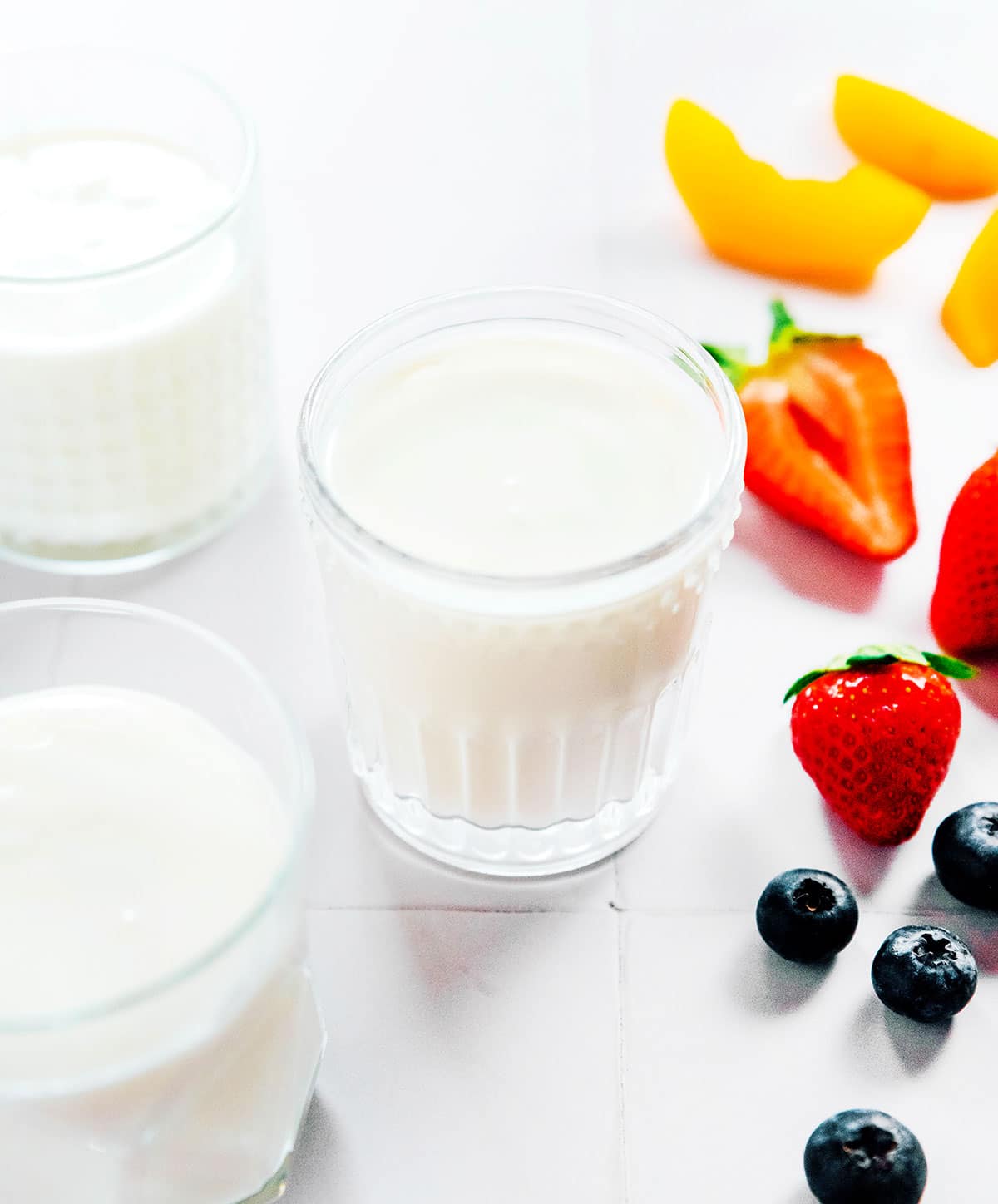 Three glasses of plain milk kefir with fresh fruit on the counter.