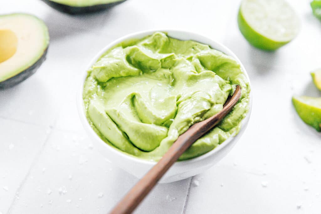 Small white bowl of avocado crema with a wooden spoon.