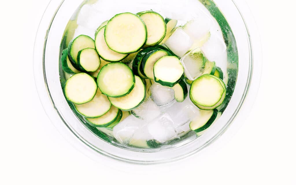 Blanched zucchini slices in a bowl of ice water.