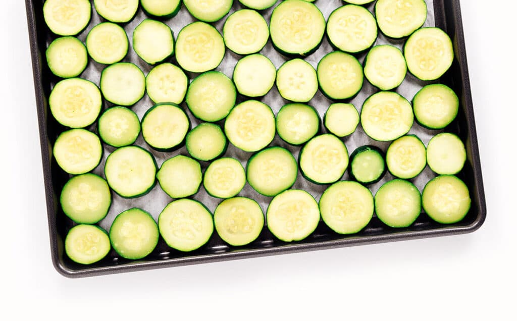 Sliced rounds of zucchini packed on a parchment paper lined baking sheet.