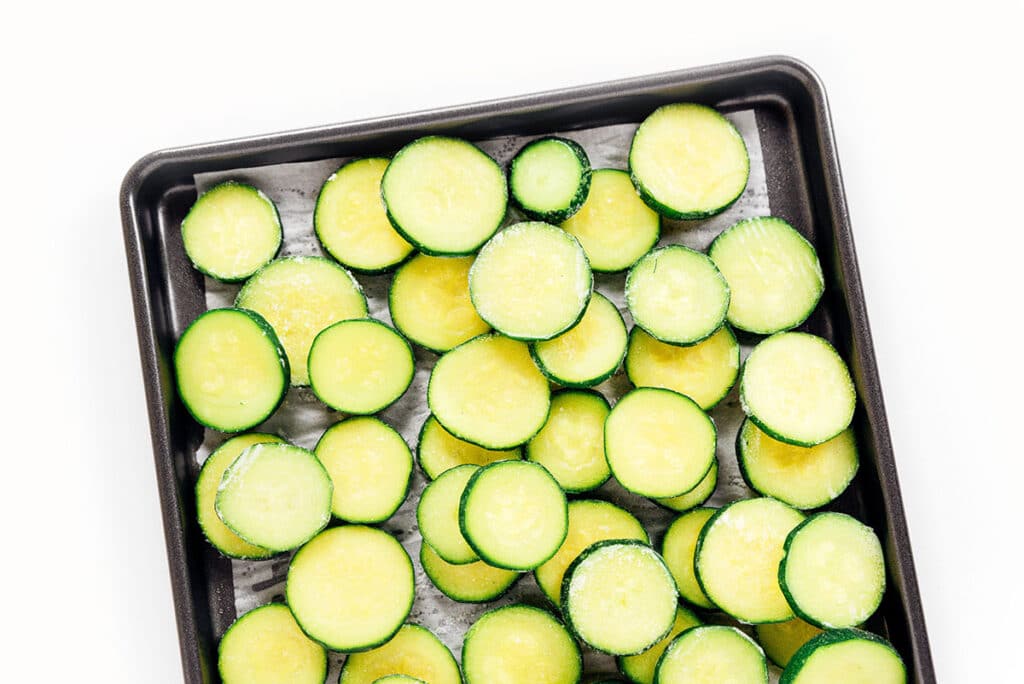 Frozen zucchini slices on a parchment lined baking sheet.
