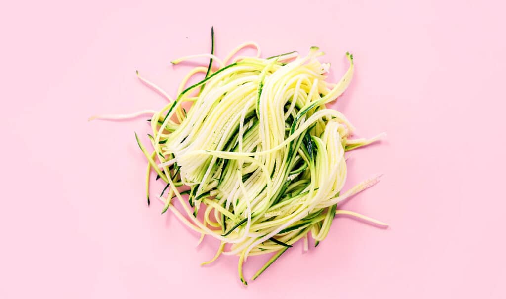 A pile of angle hair zucchini noodles on a pink background.