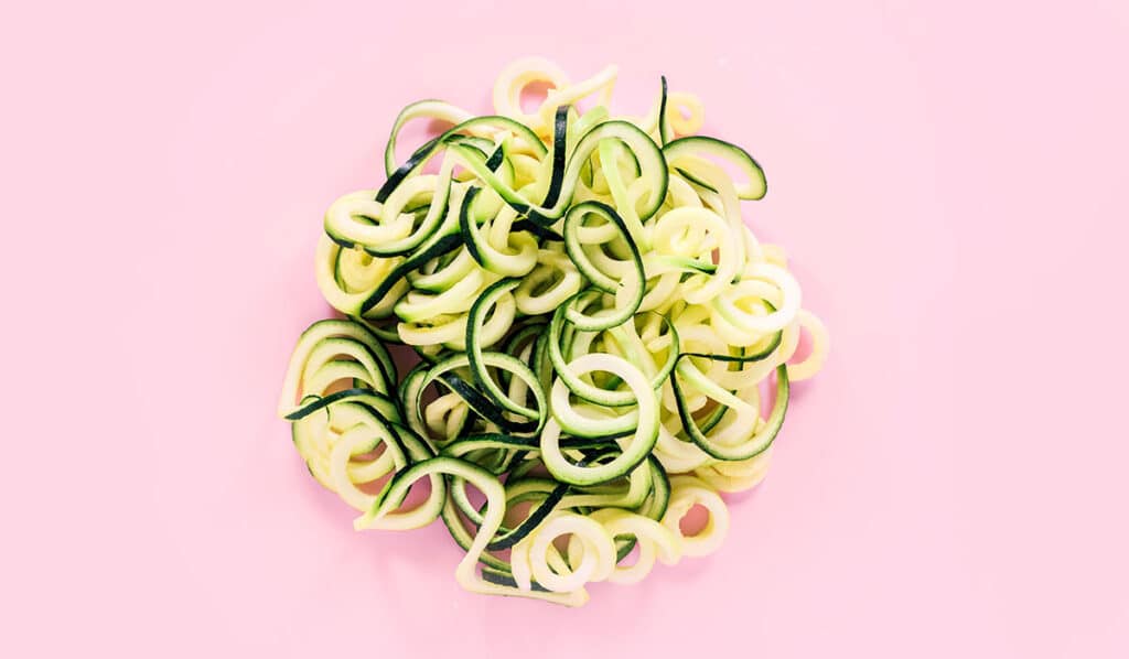 A pile of spaghetti zucchini noodles on a pink background.