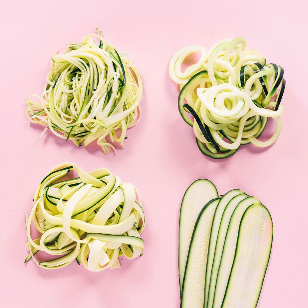 4 types of zucchini noodles on a pink background.
