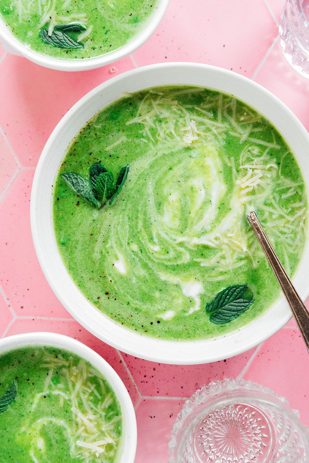 A bowl of mint pea soup in front of a pink background.