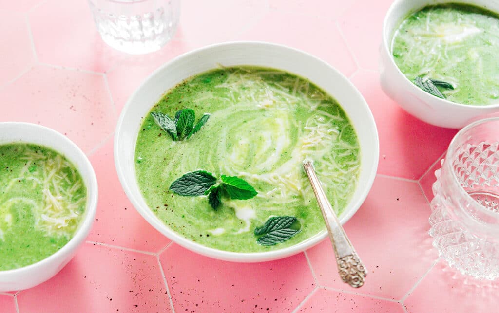 A white bowl filled with pea and mint soup between two smaller bowls filled with the same