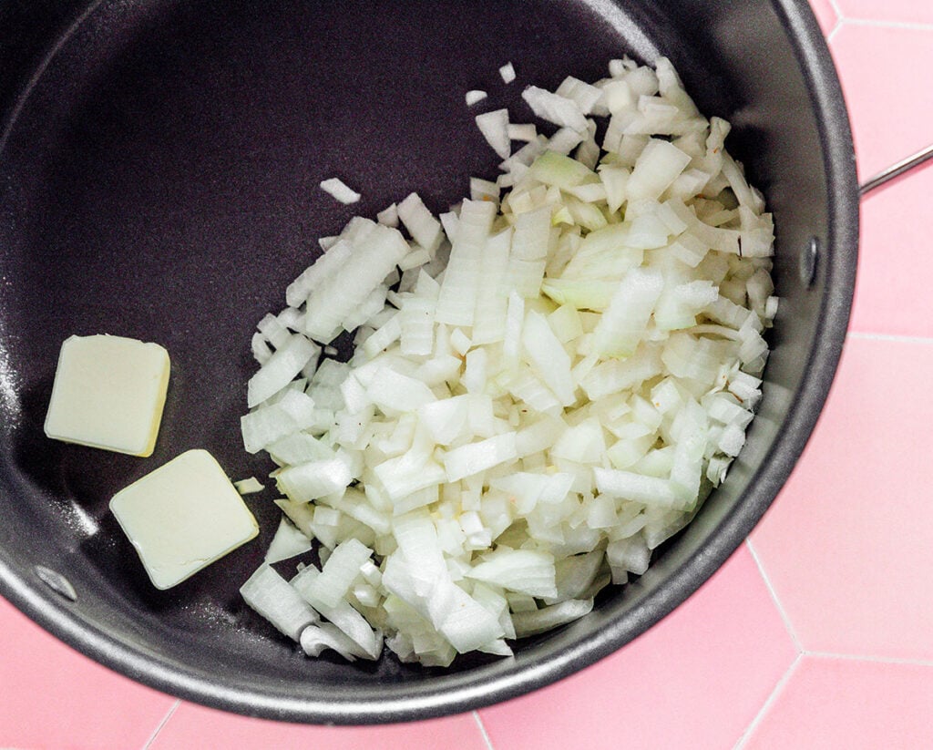 A cooking pot filled with diced white onion and a few pads of butter