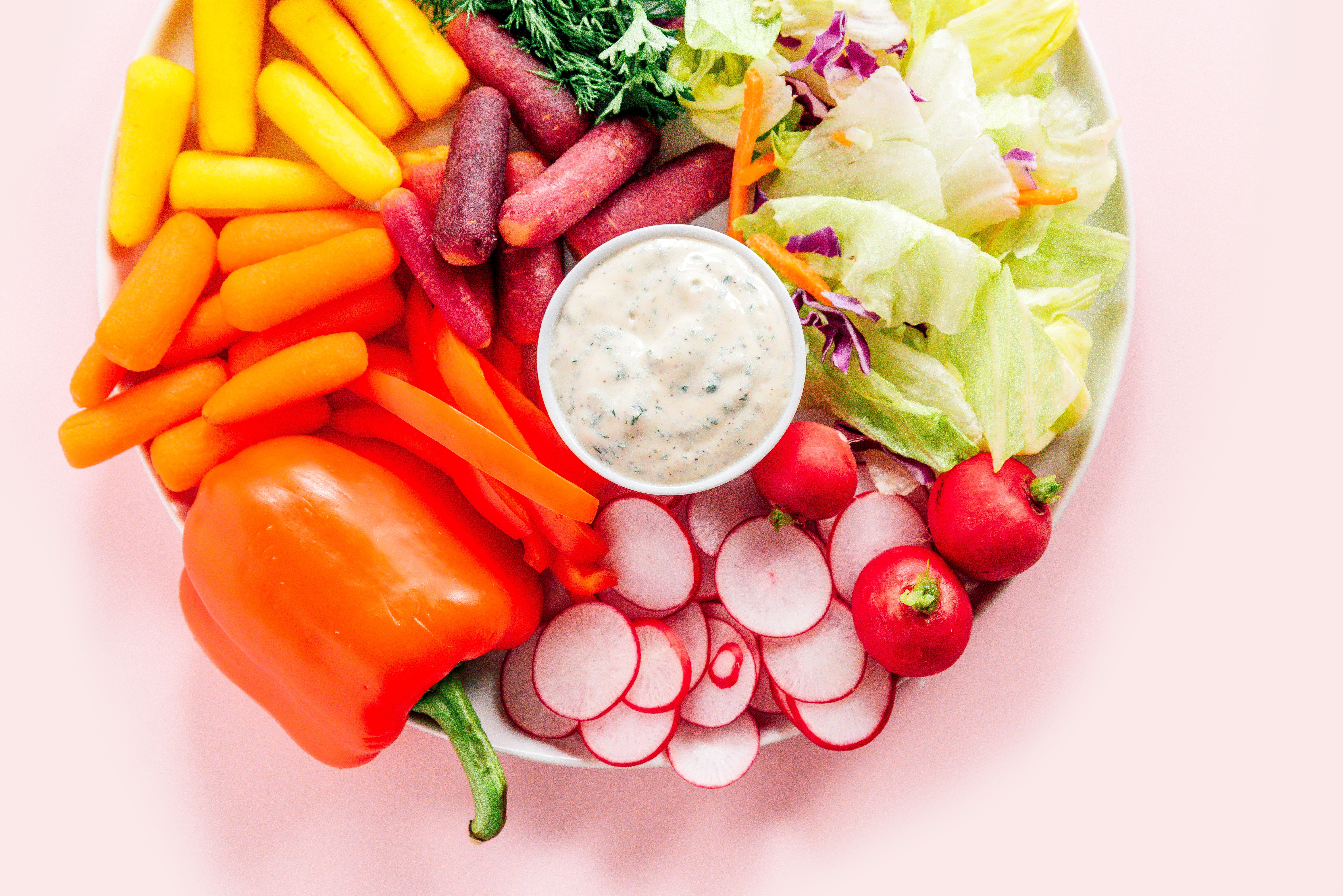 A platter filled with a bowl of homemade ranch dressing surrounded by veggies like peppers, carrots, radishes, lettuce, and more