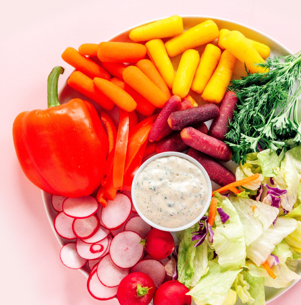 A platter filled with a bowl of tofu ranch dressing surrounded by veggies like peppers, carrots, radishes, lettuce, and more