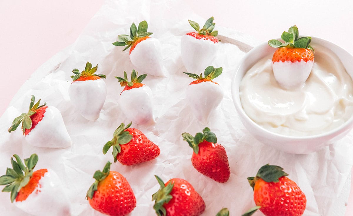 Whole fresh strawberries being dipped into a small bowl of plain yogurt.