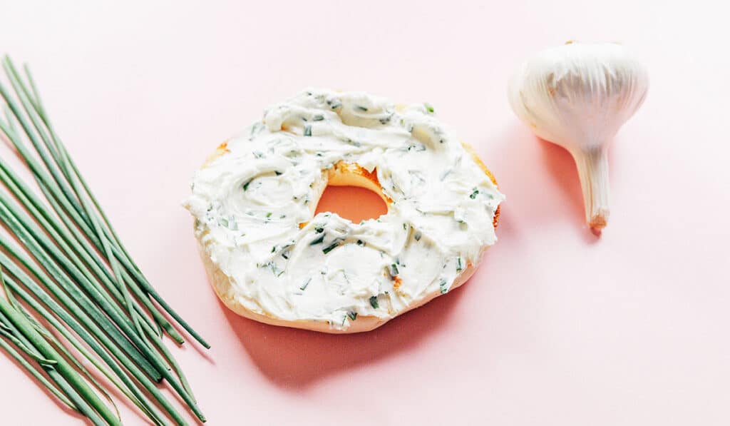 A bagel half spread with garlic and chive cream cheese.