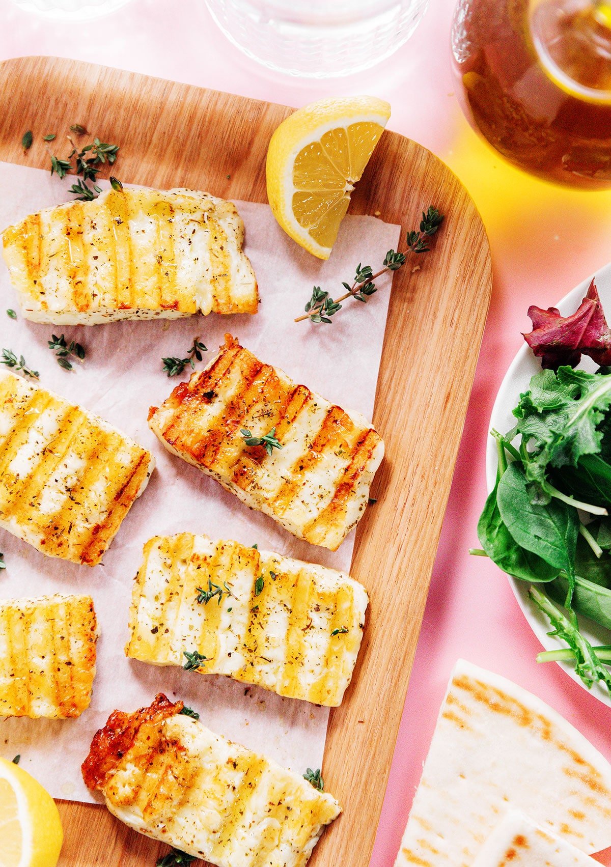 close up image of grilled halloumi with herbs and lemon wedges.