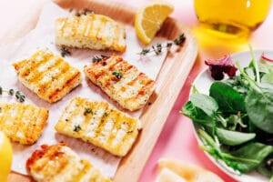 Grilled halloumi cheese slices garnished with fresh herbs, served on a wooden tray with lemon wedges and a crisp green salad—perfect for lovers of grilled halloumi.