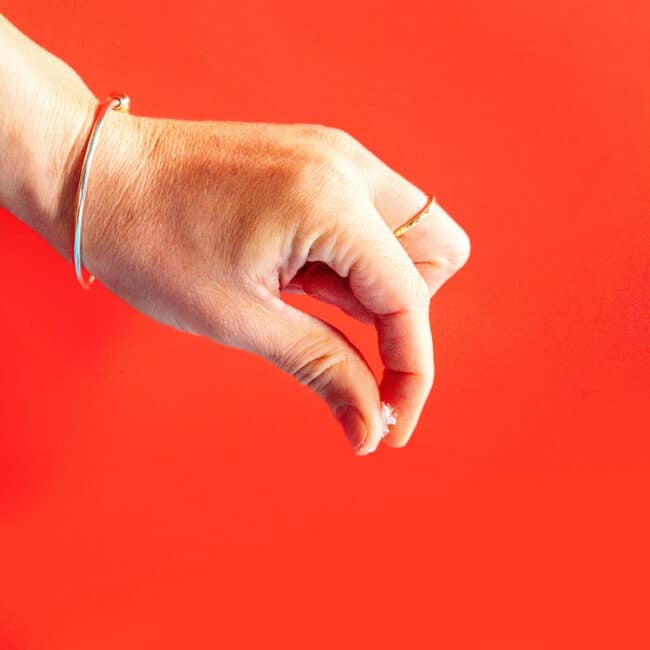 A hand holding a pinch of salt on a red background