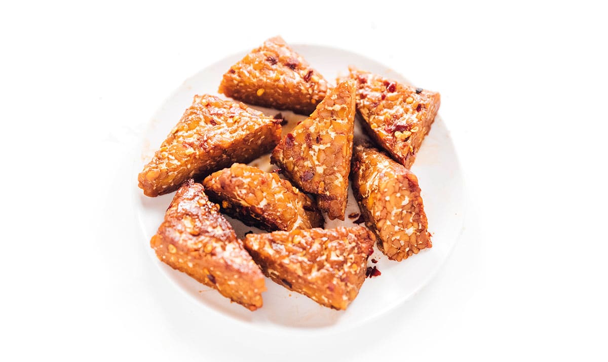 Spicy chili marinated tempeh triangles on a small white plate.