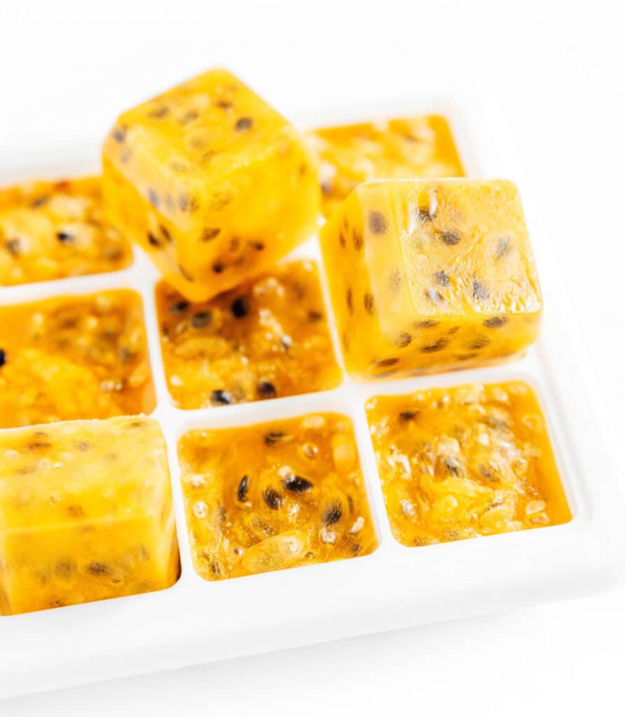 Frozen passion fruit cubes in an ice tray with 2 cubes stacked on top.